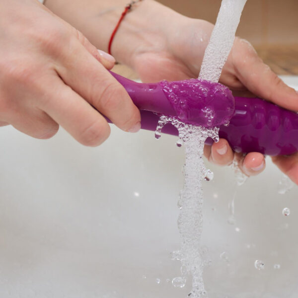 Hands cleaning a purple object under running water.