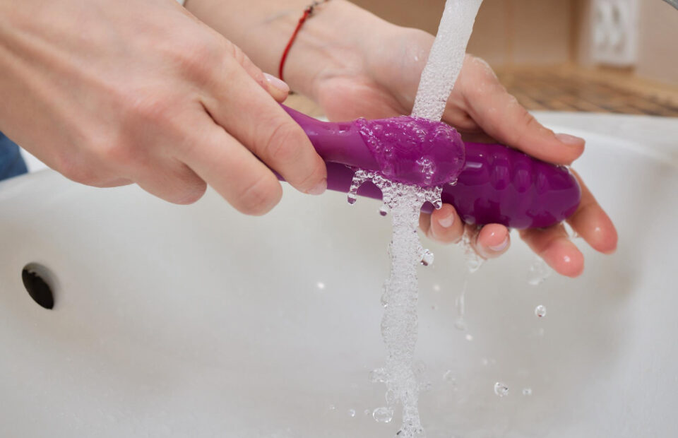 Hands cleaning a purple object under running water.